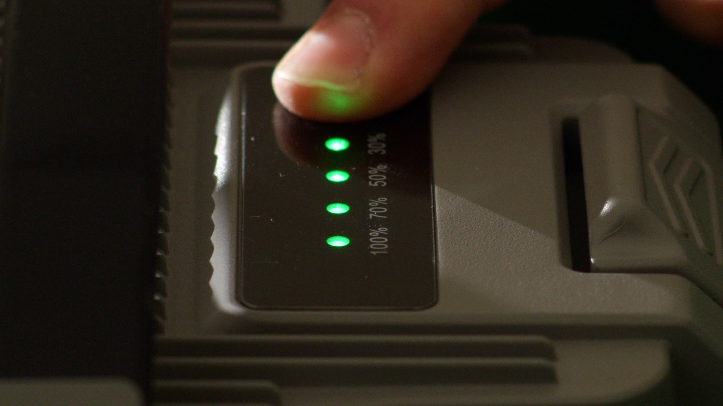 A hand pressing the power control on an I-19 battery pack, status LEDs lit green