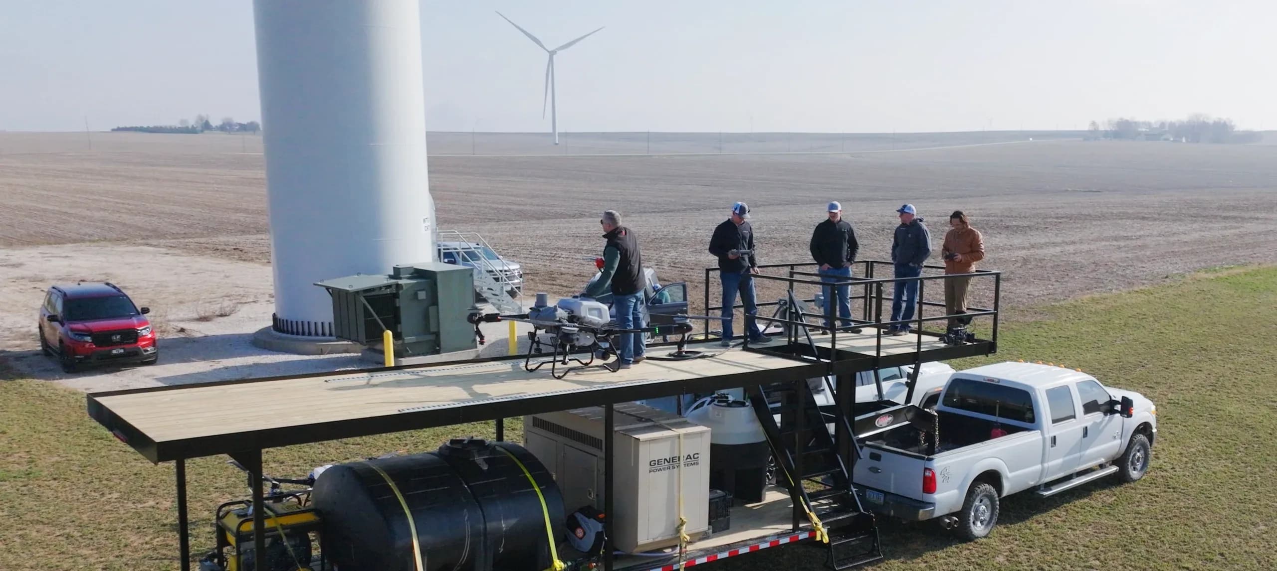 A drone tendering rig in the field: a two-level trailer with a flight deck, spray drone, on-board water tank and generator, and the crew on deck